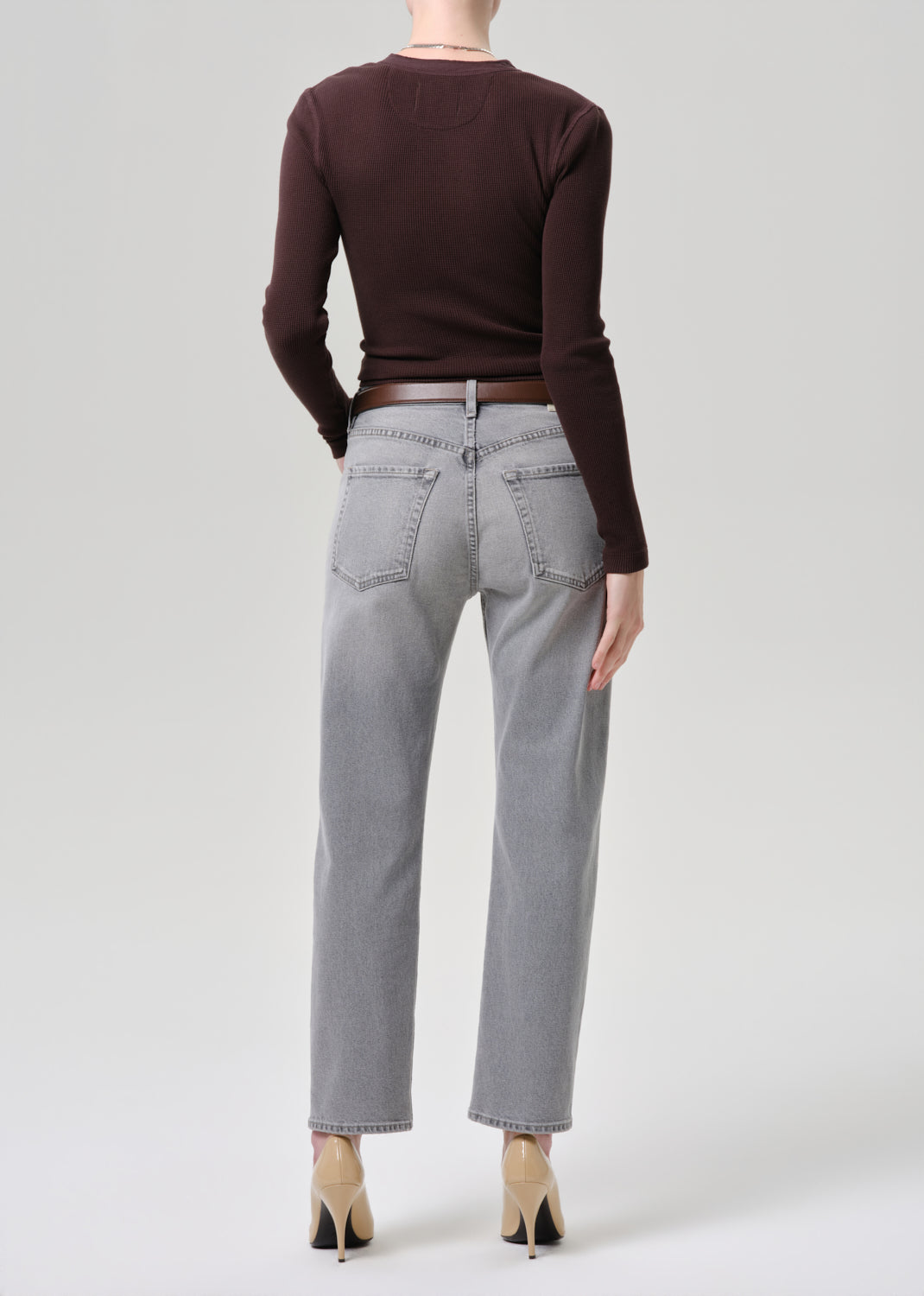 Person wearing a brown sweater and gray jeans on a grey background