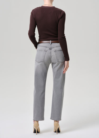Person wearing a brown sweater and gray jeans on a grey background