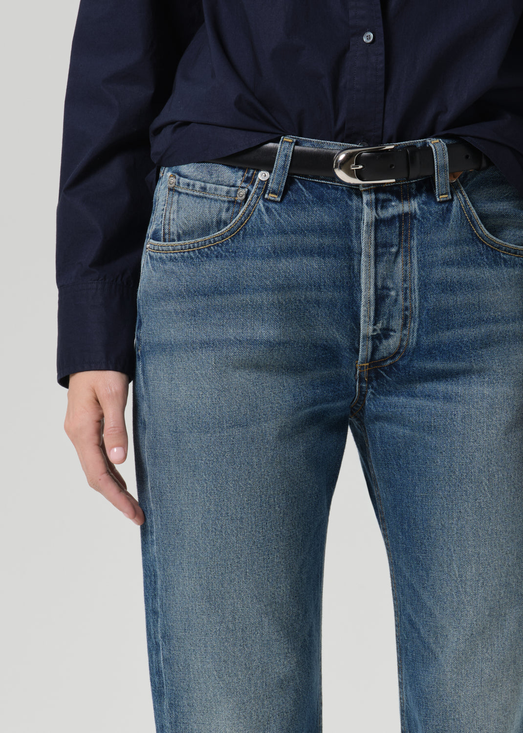Close-up of medium wash straight leg jeans with a navy long sleeve button front blouse on a grey background