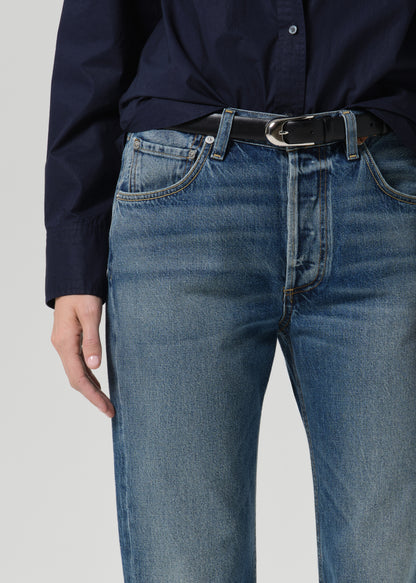 Close-up of medium wash straight leg jeans with a navy long sleeve button front blouse on a grey background