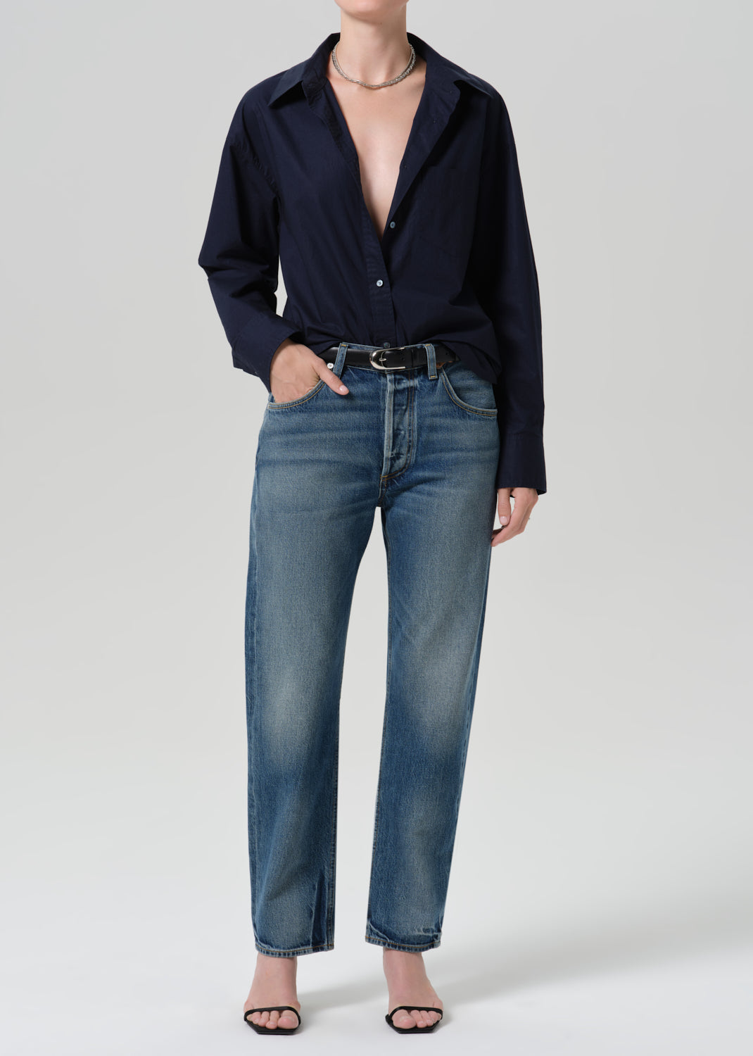 Person wearing a navy long sleeve button front blouse with medium wash straight leg jeans on a grey background