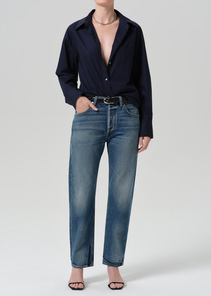 Person wearing a navy long sleeve button front blouse with medium wash straight leg jeans on a grey background