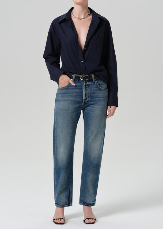 Person wearing a navy long sleeve button front blouse with medium wash straight leg jeans on a grey background