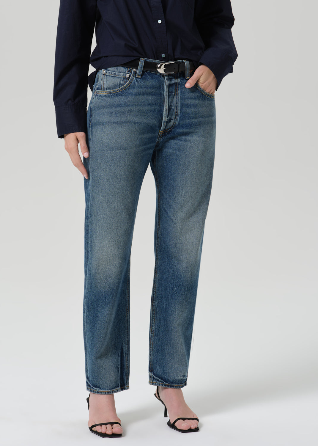 Person wearing a navy long sleeve button front blouse with medium wash straight leg jeans on a grey background