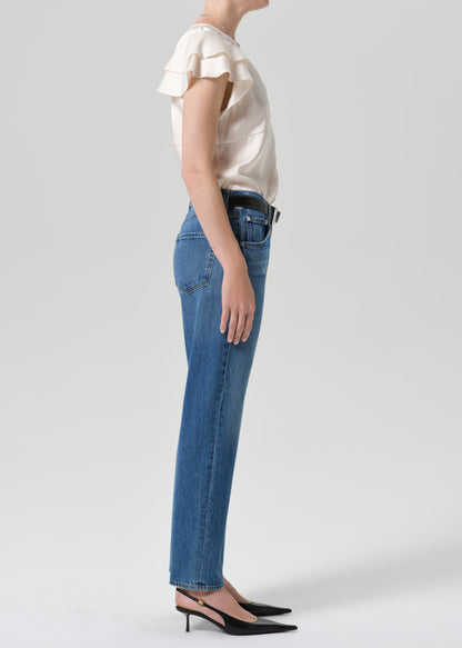 Person wearing medium wash straight leg jeans with a white short sleeve blouse viewed from the side on a grey background