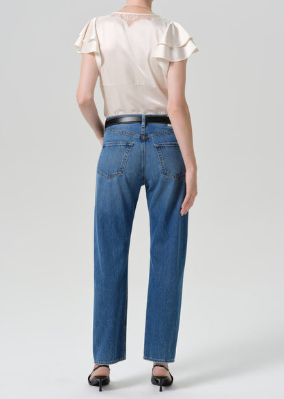 Person wearing medium wash straight leg jeans with a white short sleeve blouse viewed from the back on a grey background
