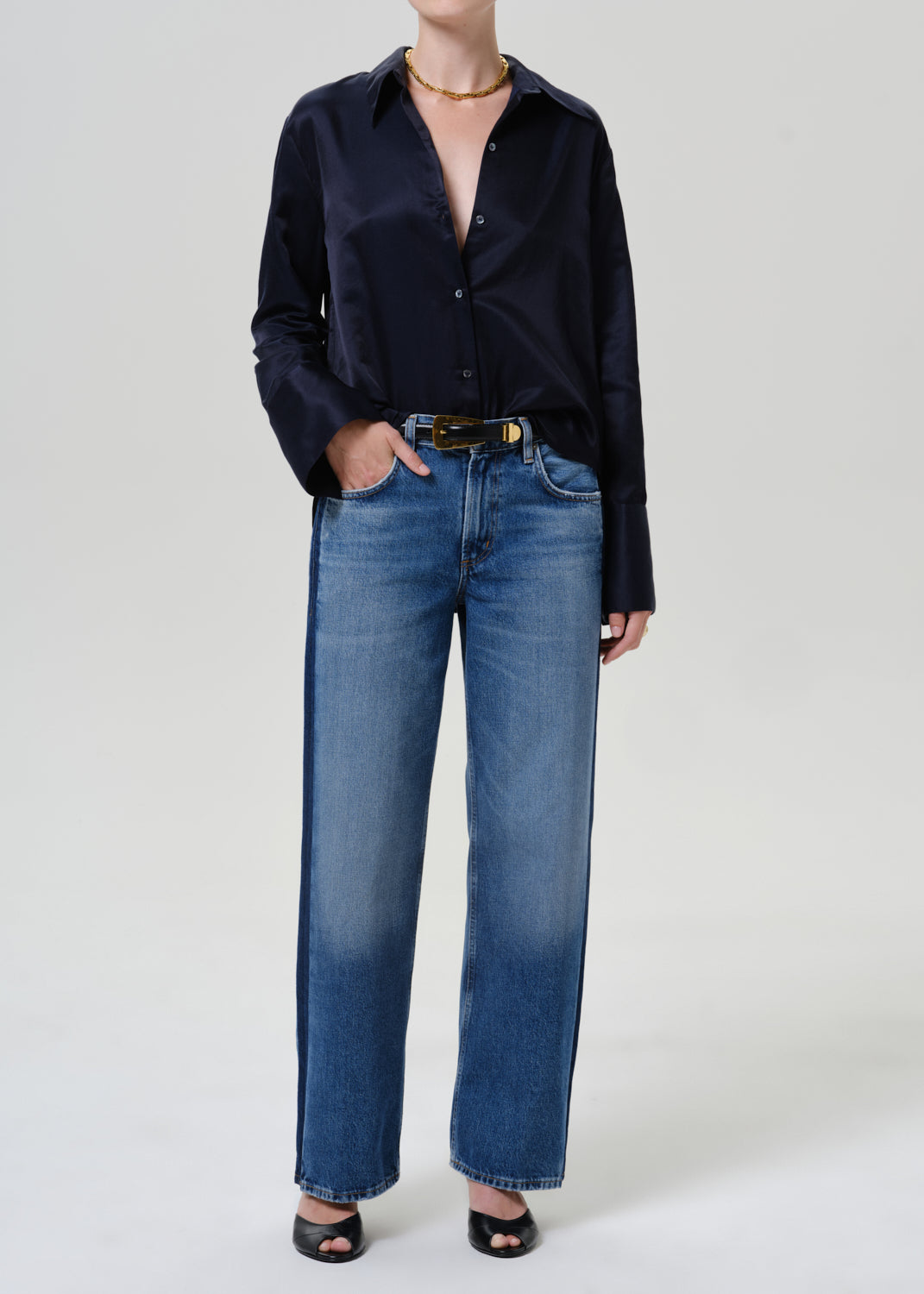 Woman wearing medium blue wide leg jeans with a dark navy button-up shirt on a grey background.