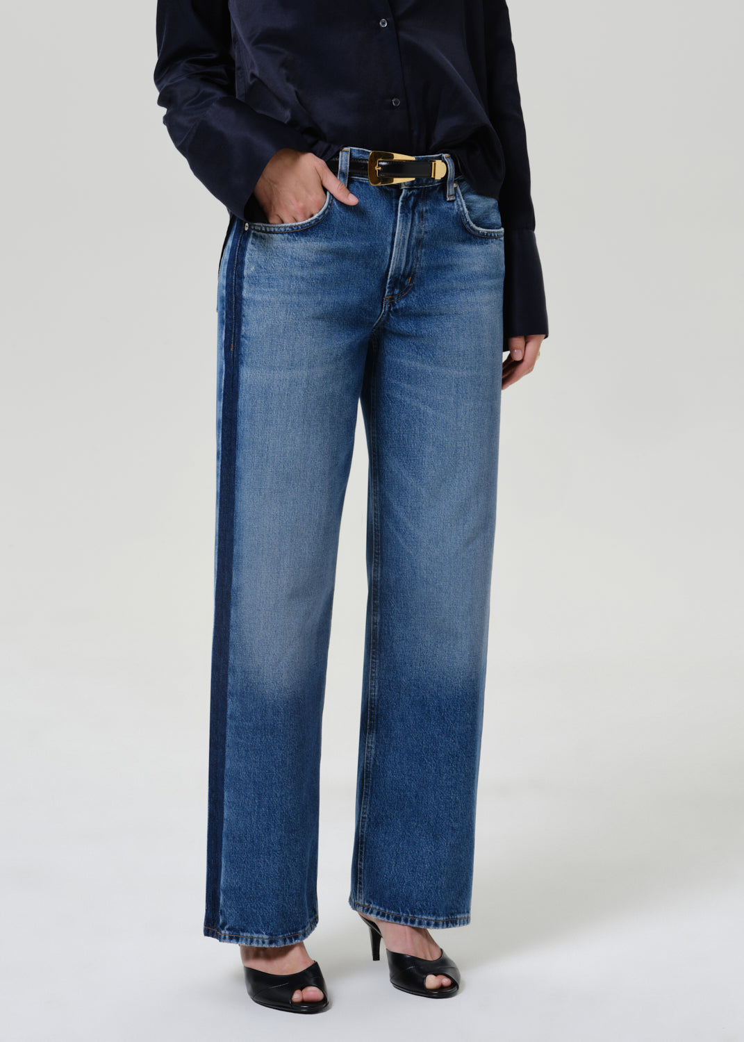 Woman wearing medium blue wide leg jeans with a dark navy button-up shirt on a grey background.
