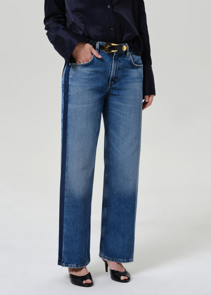 Woman wearing medium blue wide leg jeans with a dark navy button-up shirt on a grey background.