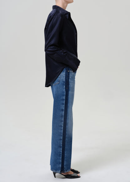 Woman wearing medium blue wide leg jeans with a dark navy button-up shirt viewed from the side on a grey background.