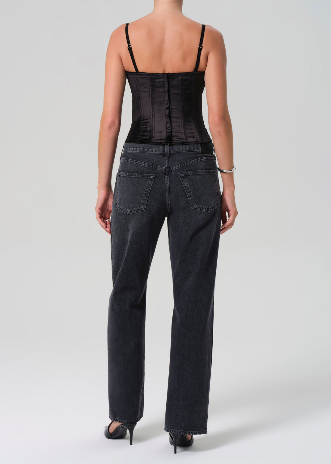 Person wearing a black corset and black jeans on a greybackground