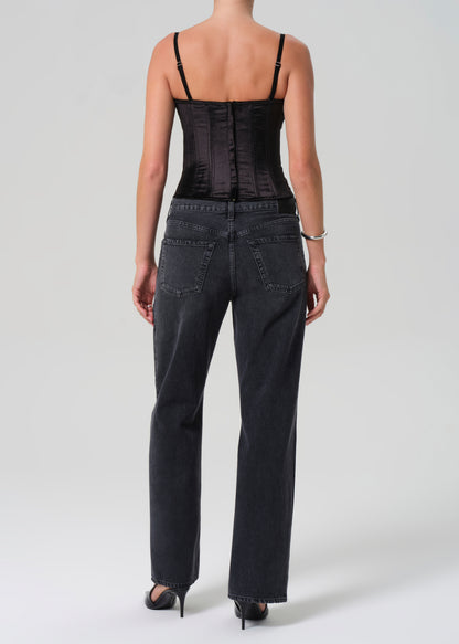 Person wearing a black corset and black jeans on a greybackground