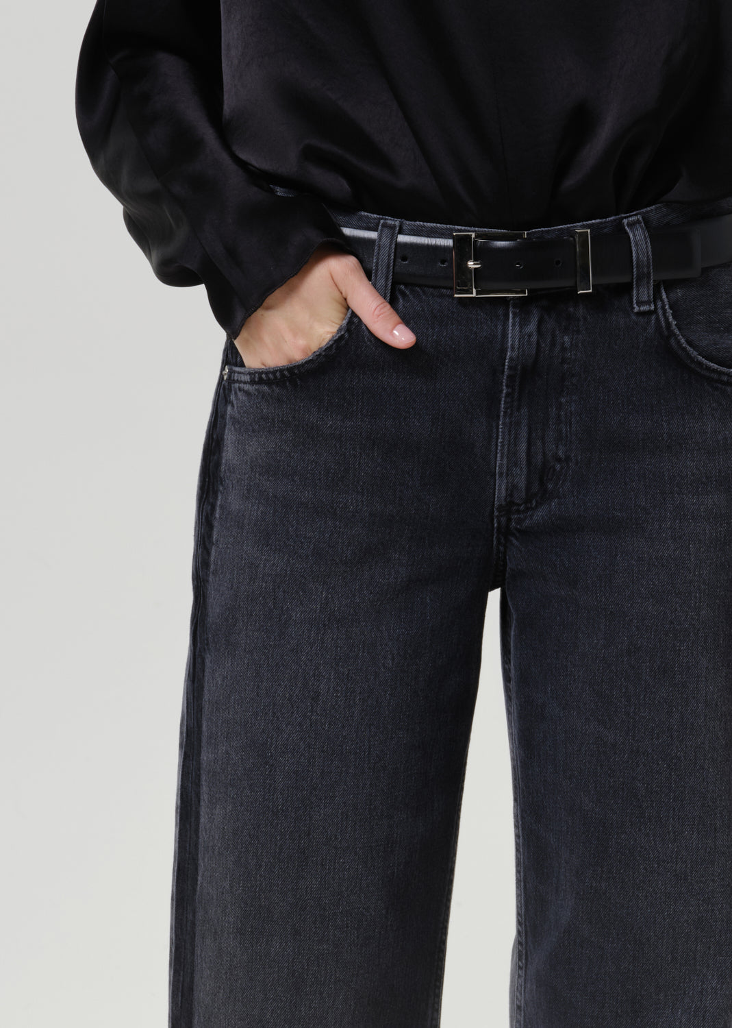 Close-up of dark grey wide leg jeans on a grey background.