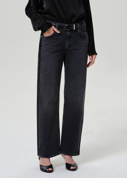 Woman wearing dark grey wide leg jeans with a black draped neck top on a grey background.