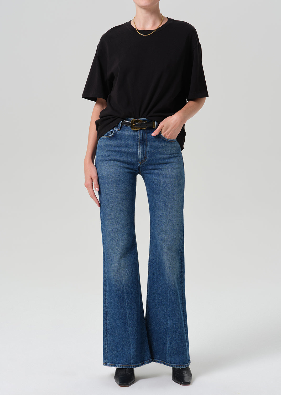 A model wearing a black oversized t-shirt and blue wide-leg flare jeans, standing against a grey background.