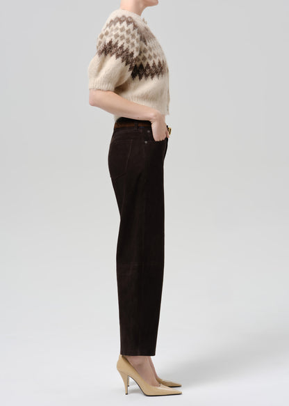 Person wearing a cream and brown patterned short sleeve cardigan with dark brown straight leg trousers viewed from the side on a grey background