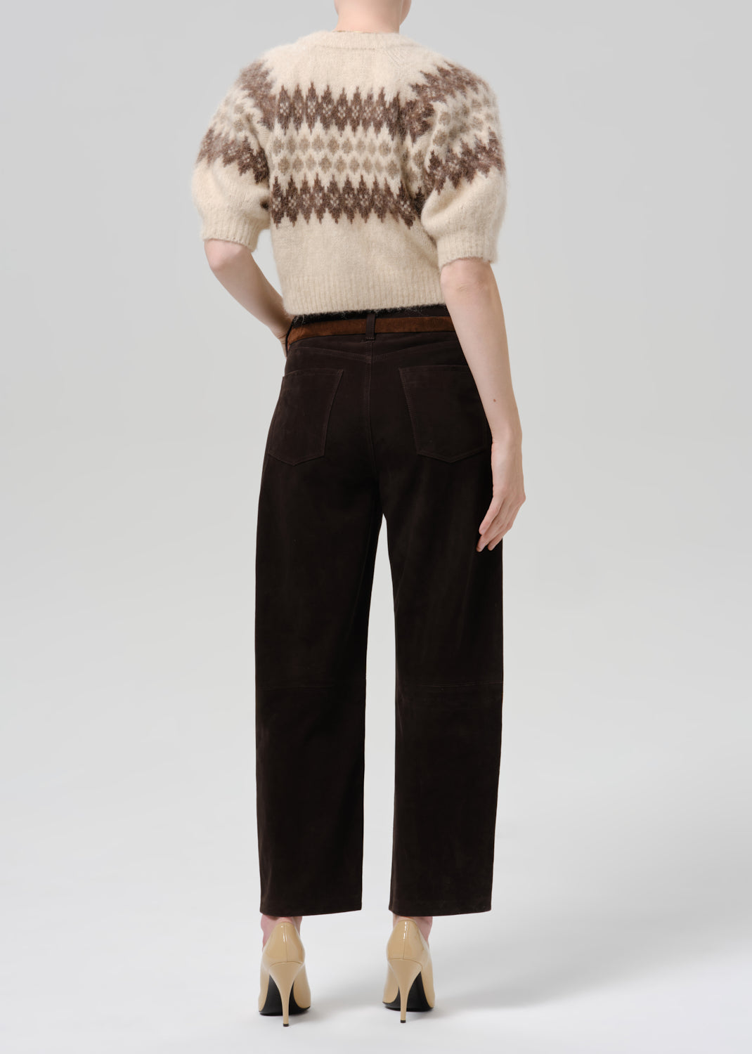 Person wearing a cream and brown patterned short sleeve cardigan with dark brown straight leg trousers viewed from the back on a grey background
