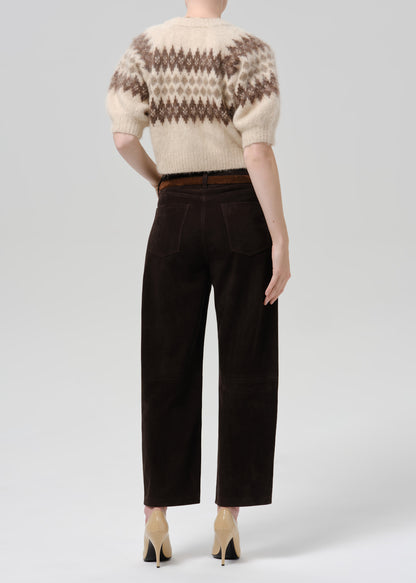 Person wearing a cream and brown patterned short sleeve cardigan with dark brown straight leg trousers viewed from the back on a grey background
