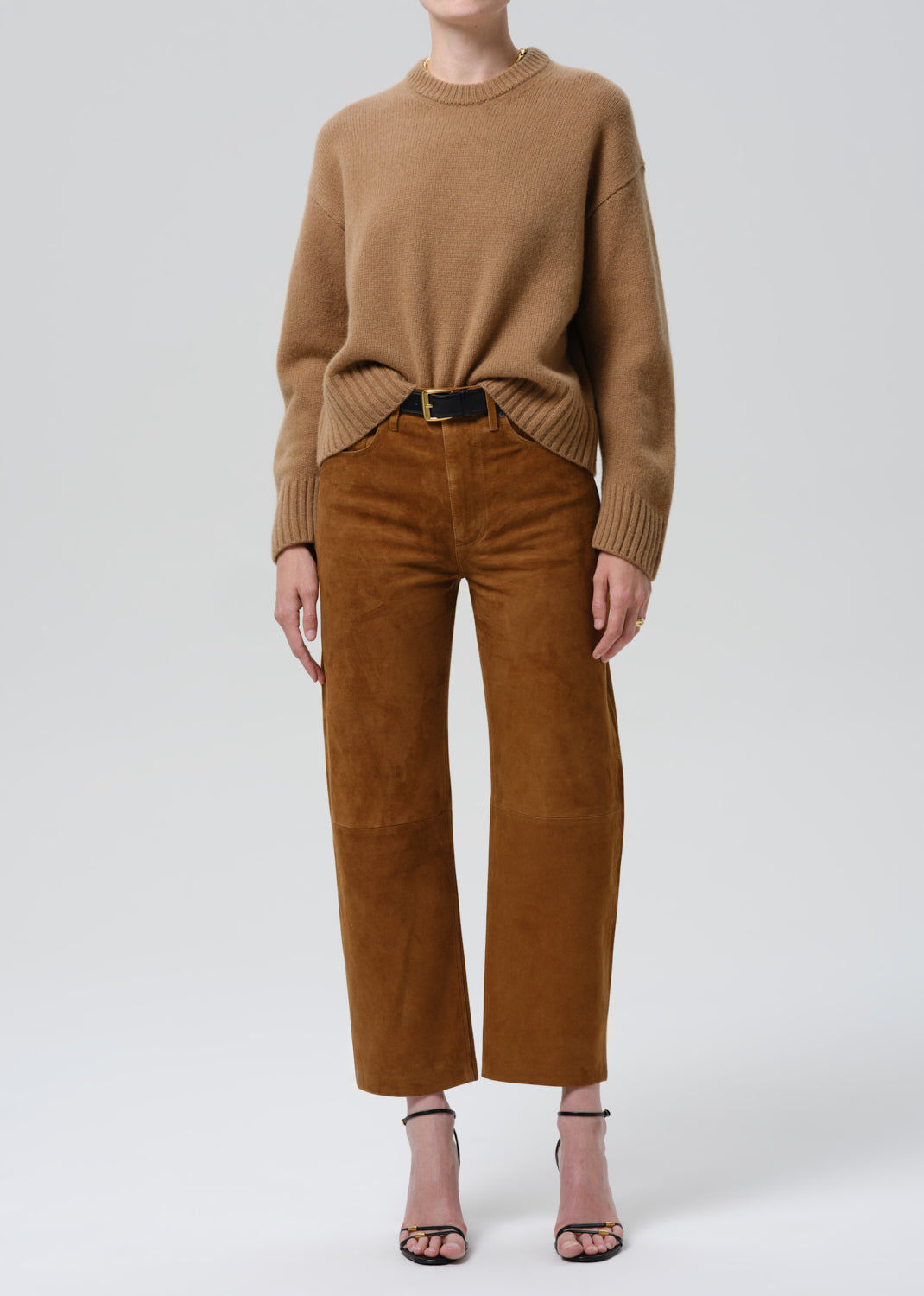 Person wearing a brown sweater and matching pants on a grey background.
