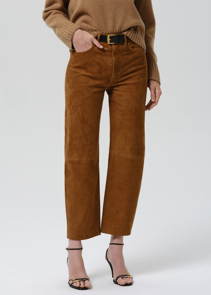 A model is shown from the waist down wearing brown wide-leg cropped trousers made of a soft suede-like fabric, paired with a black belt, a beige sweater, and black strappy high-heeled sandals against a grey background.