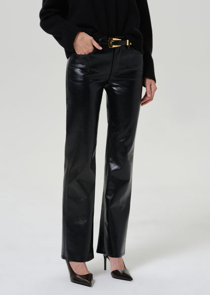 A model wearing shiny black wide-leg pants with a black belt and black pointed-toe heels, shown from the chest down against a light gray studio background.