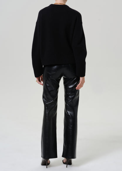 A model shown from the back wearing a black knit sweater and shiny black leather flare pants, paired with black high heels, against a light gray studio background.