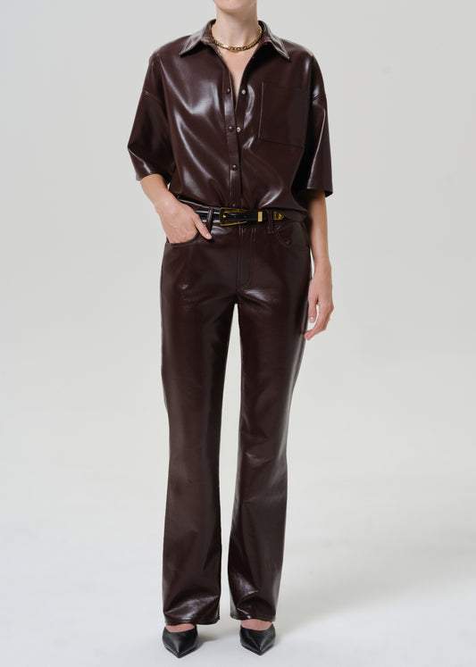 Person wearing dark burgundy leather straight leg pants with a matching short sleeve leather shirt, black belt with gold buckle, and black pointed-toe heels, front full body view on a grey background.