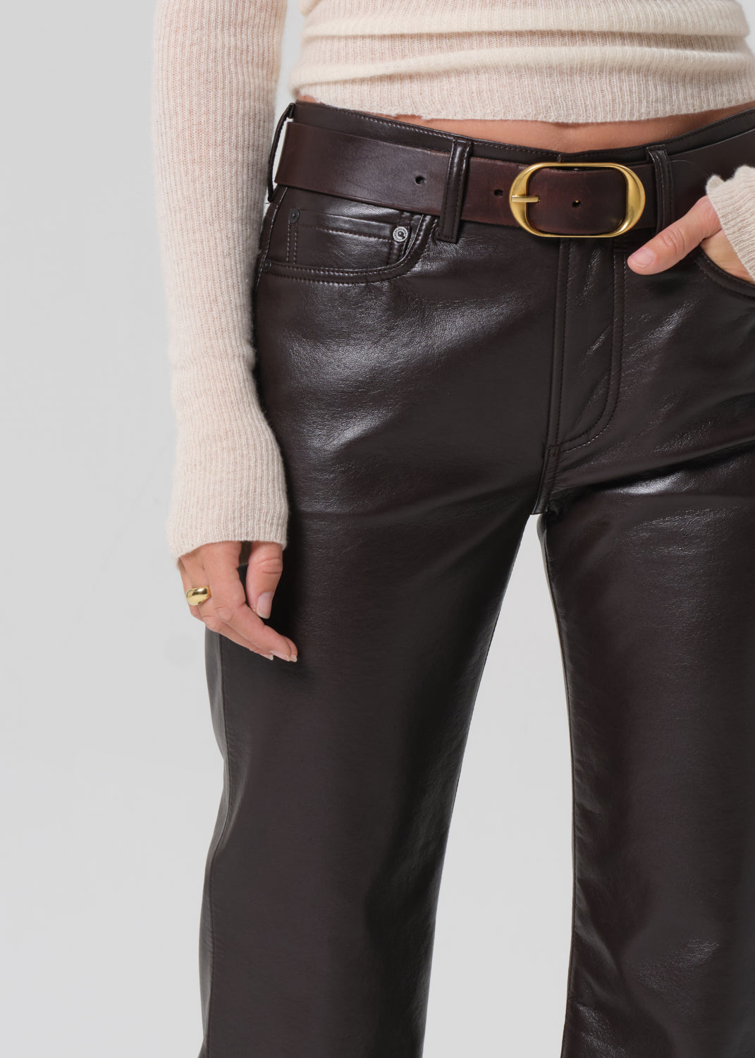 Person wearing brown leather pants with a beige sweater on a light gray background