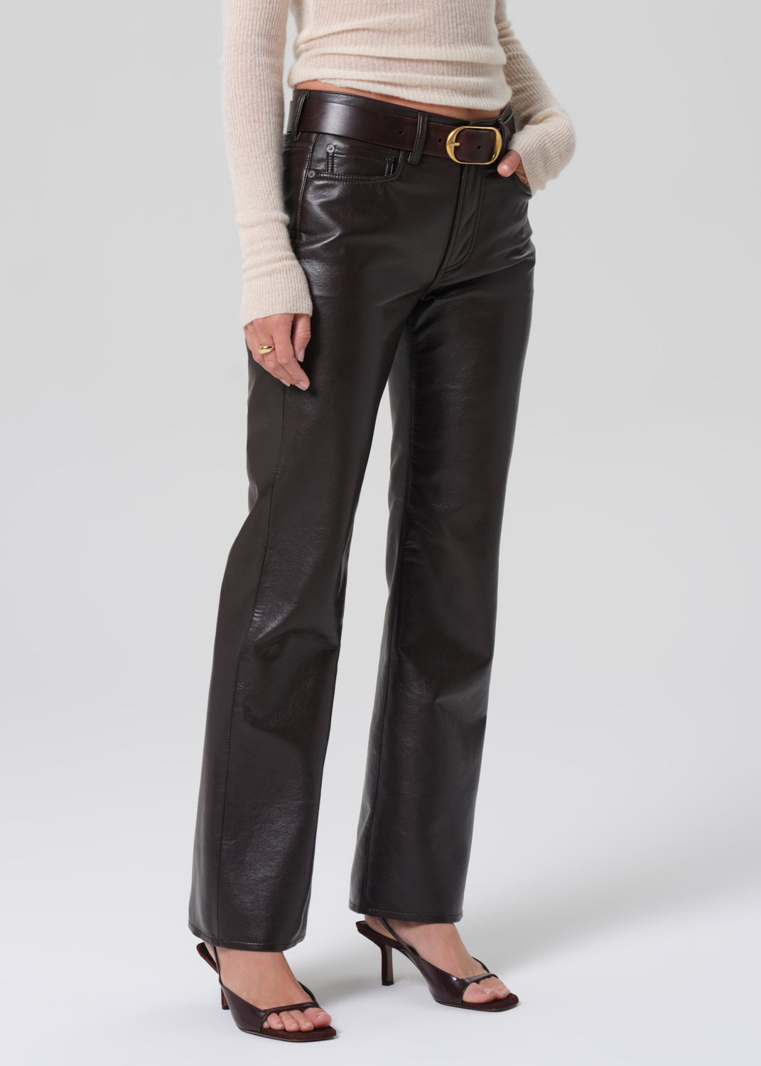 Person wearing brown leather pants with a beige sweater on a white background