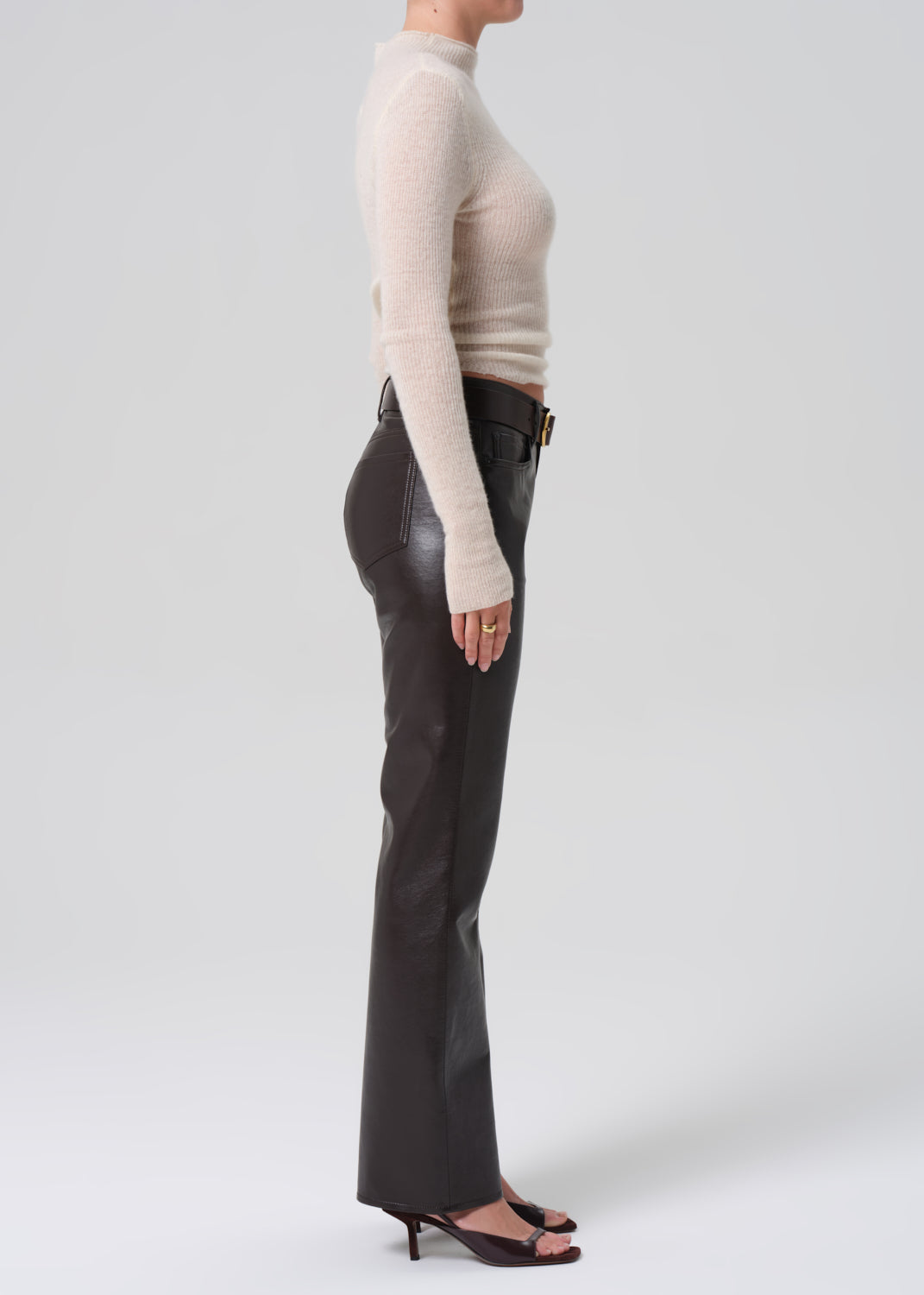 Person wearing a beige sweater and brown leather pants on a white background