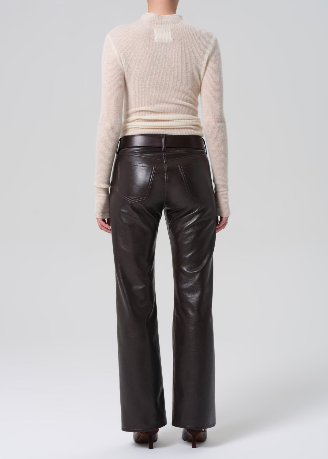 Person wearing a beige sweater and brown leather pants on a white background