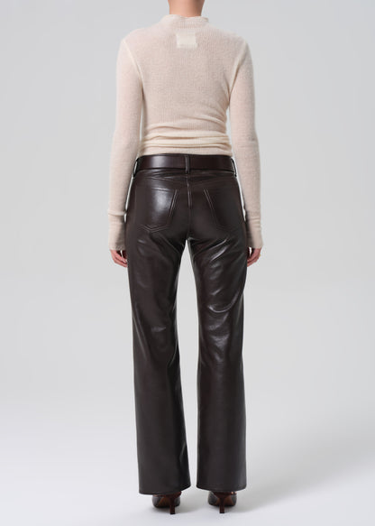 Person wearing a beige sweater and brown leather pants on a white background