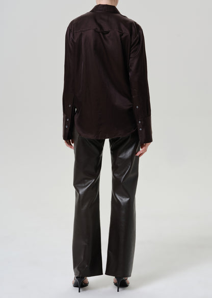 A model shown from the back wearing a dark brown long-sleeve button-down shirt and shiny black wide-leg trousers, paired with black high heels, against a light gray studio background.