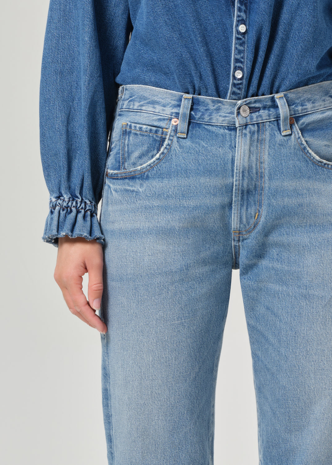 Person wearing a blue denim shirt and jeans on a plain background