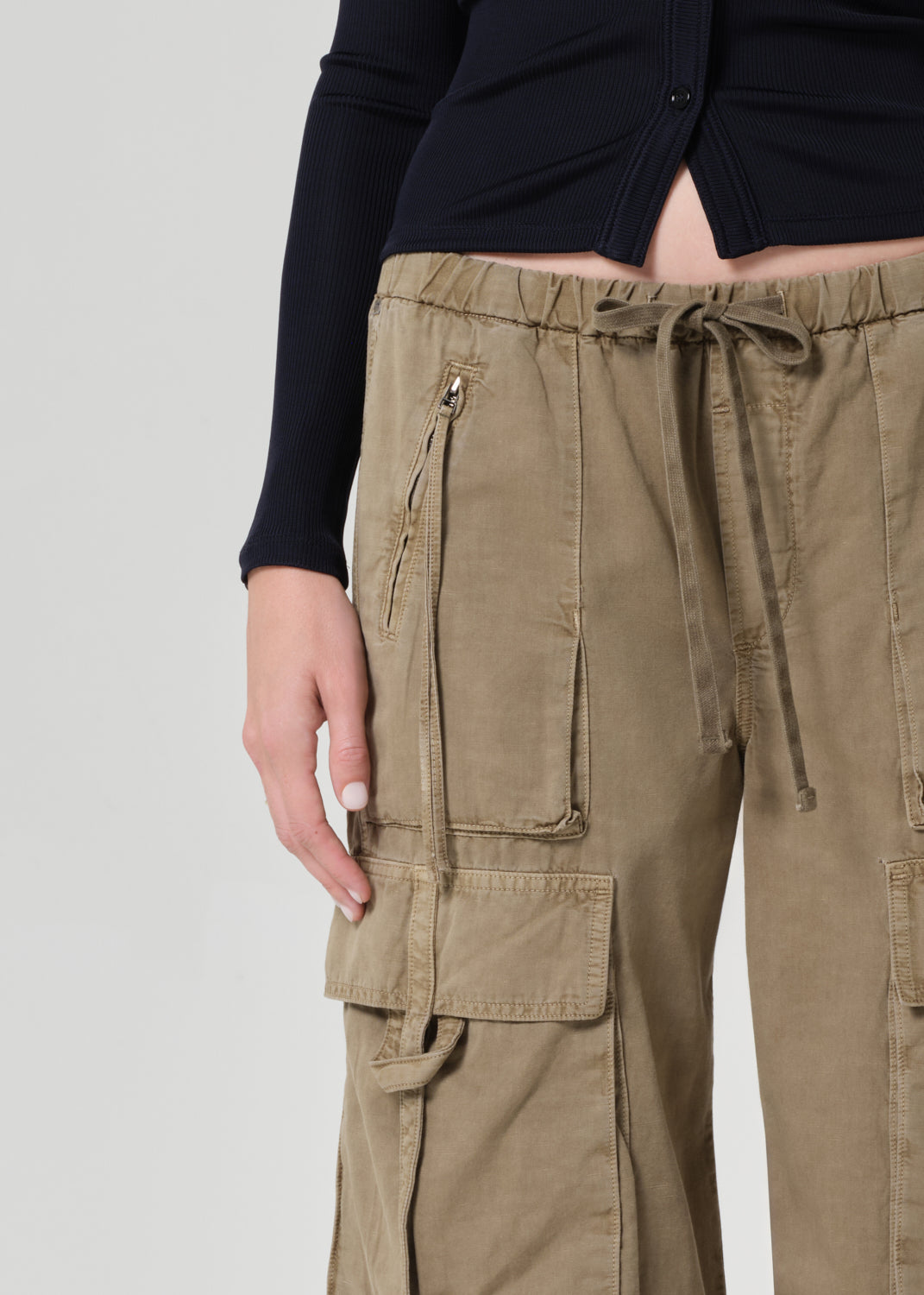 Person wearing a black shirt and beige cargo pants on a plain background