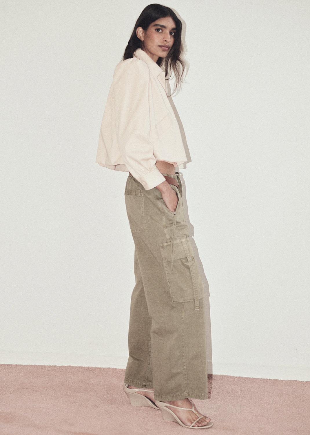 Woman wearing a light jacket and beige cargo pants against a plain background