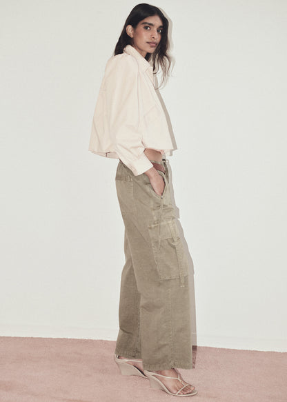 Woman wearing a light jacket and beige cargo pants against a plain background