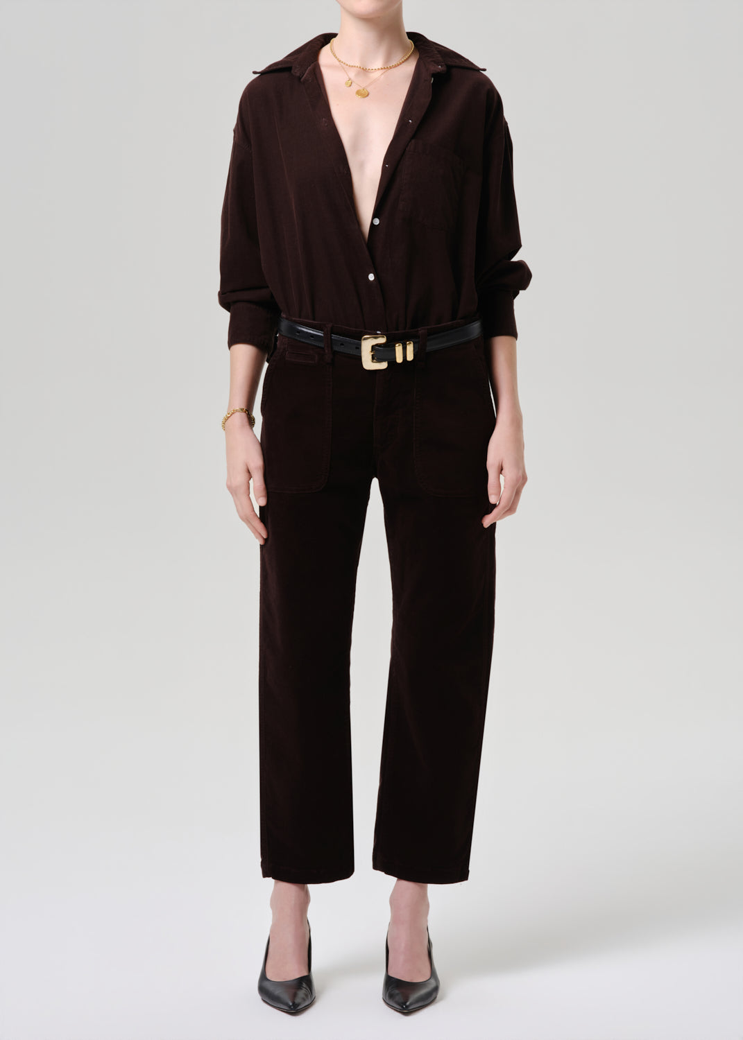 Person wearing a brown button-up shirt and black pants on a grey background