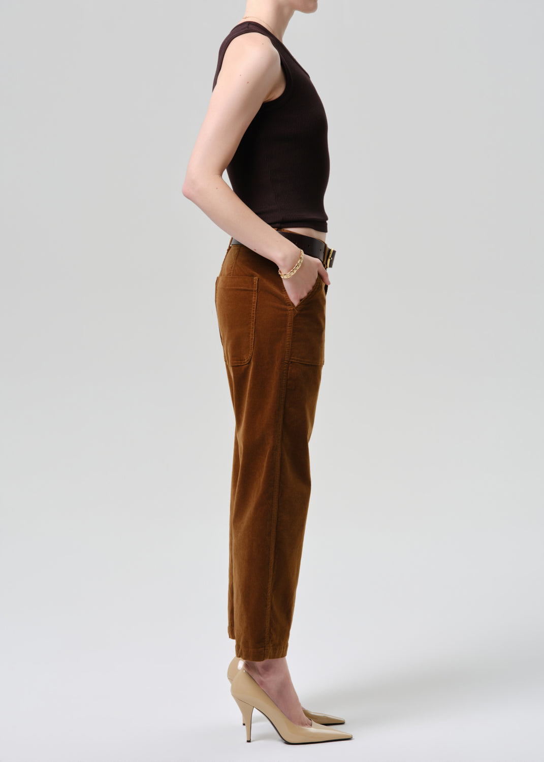 Person wearing a brown sleeveless top and brown pants on a grey background