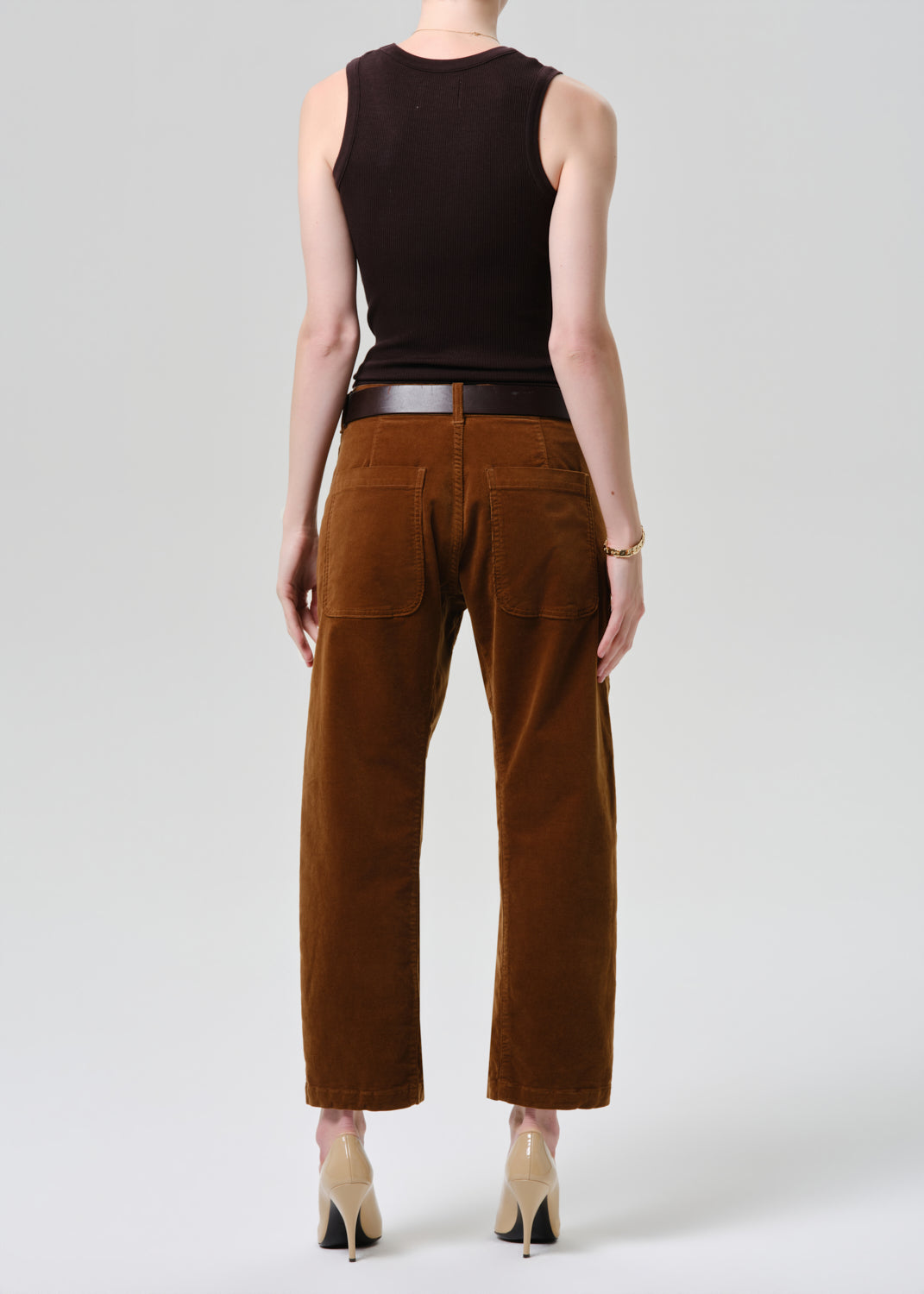 Person wearing a brown sleeveless top and brown pants on a grey background