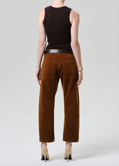 Person wearing a brown sleeveless top and brown pants on a grey background