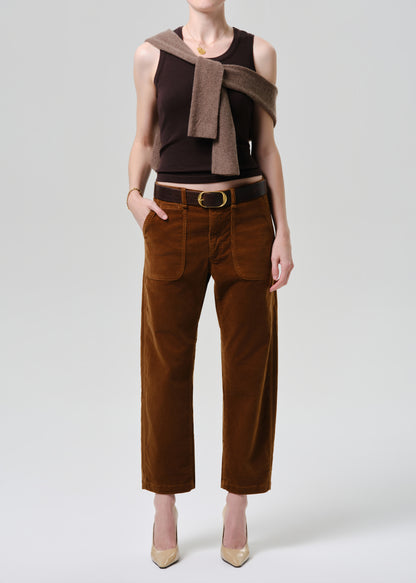 Person wearing a brown sleeveless top and pants with a belt on a grey background