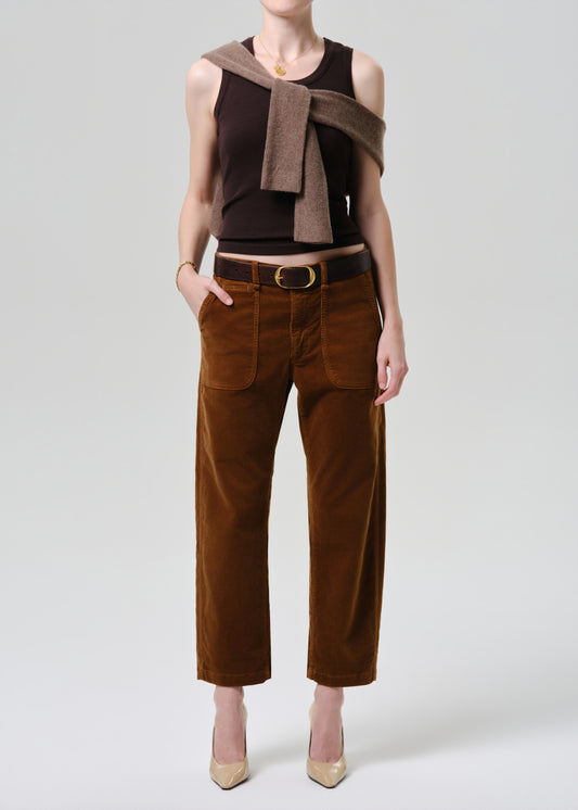 Person wearing a brown sleeveless top and pants with a belt on a grey background