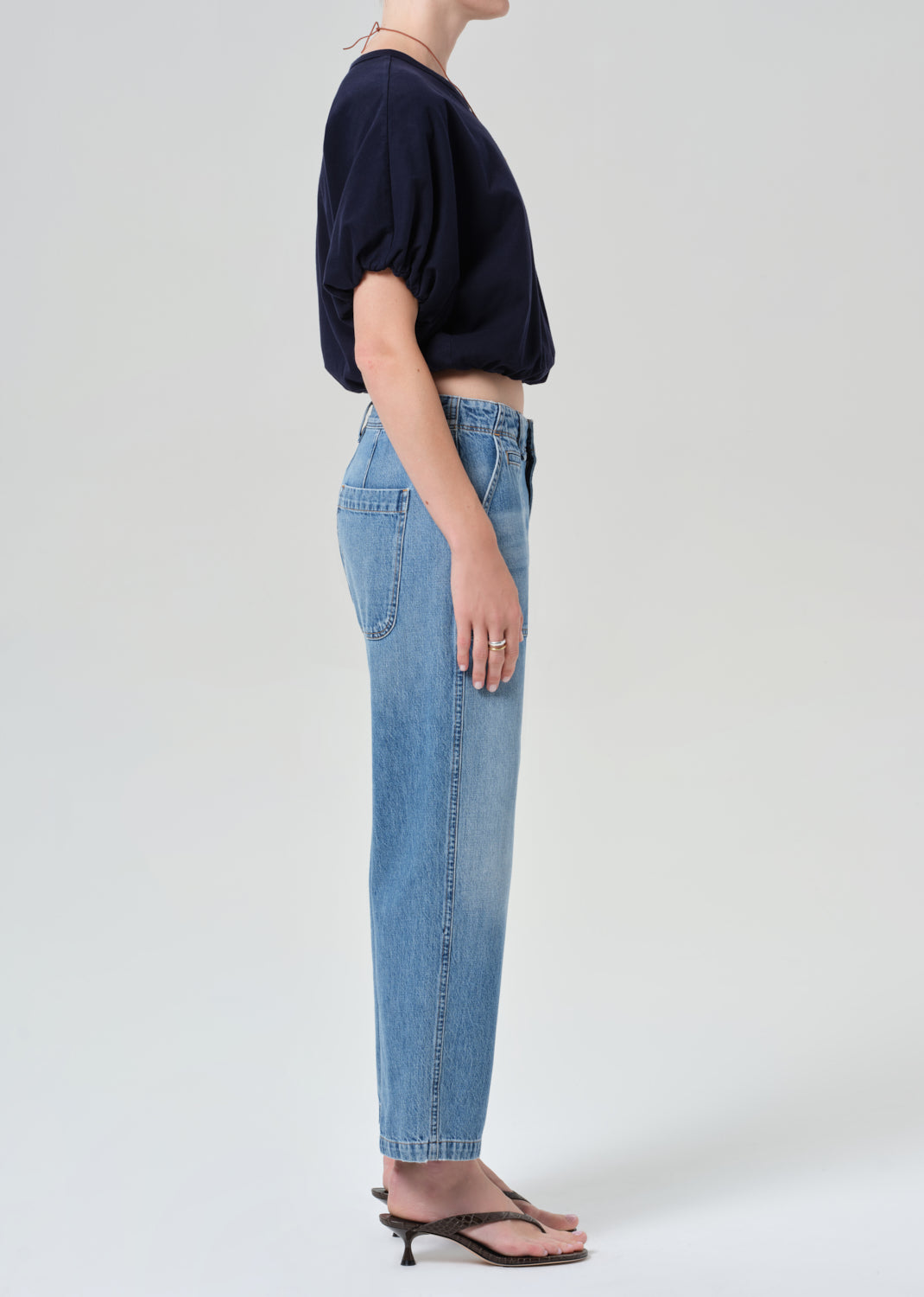 Person wearing a navy top and light blue jeans on a grey background