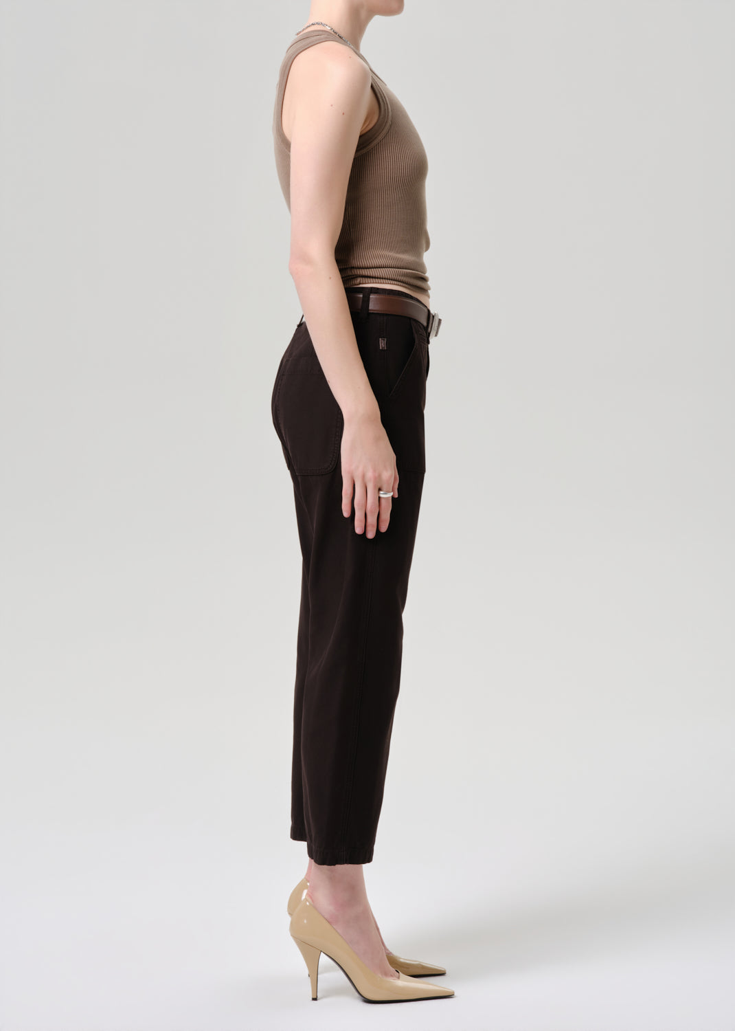Person wearing a brown sleeveless top and black pants on a grey background