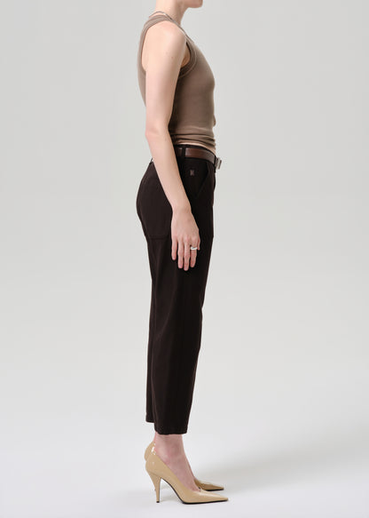 Person wearing a brown sleeveless top and black pants on a grey background