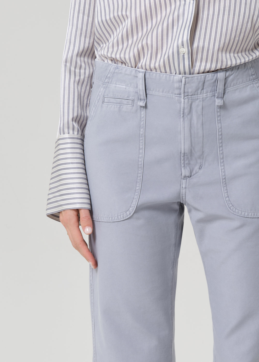 Person wearing a striped shirt and light gray pants on a grey background