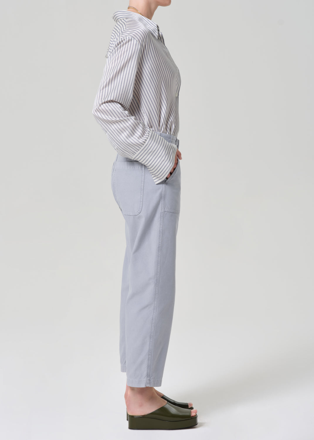 Person wearing a striped shirt and light gray pants on a grey background