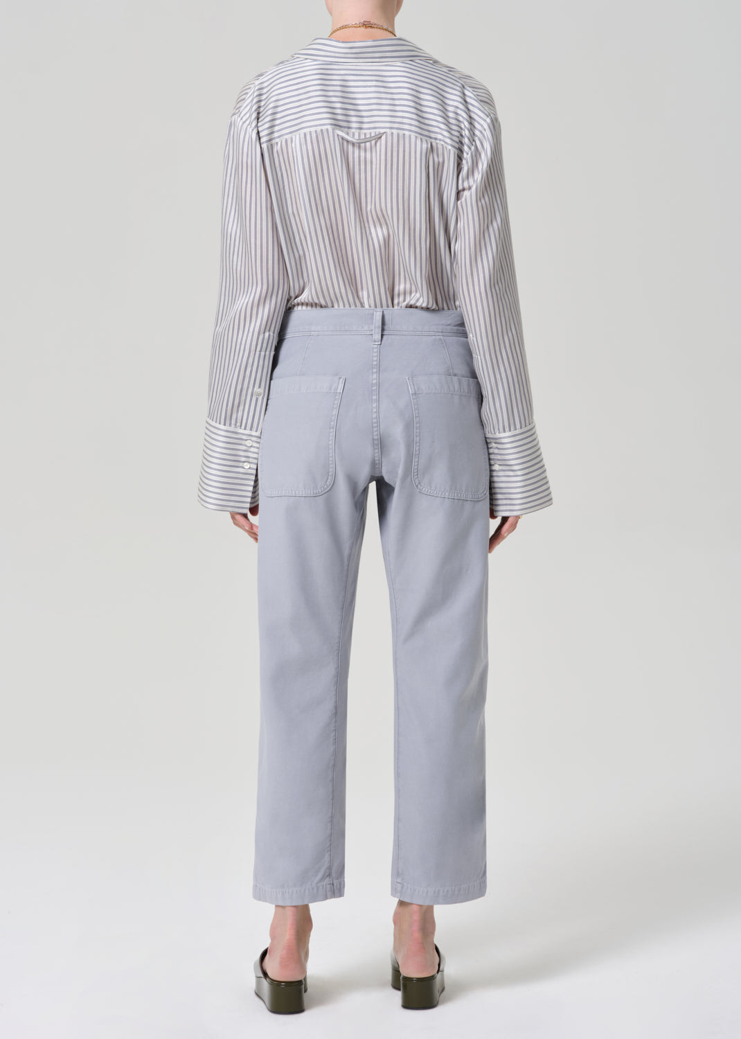 Person wearing a striped shirt and light gray pants on a grey background