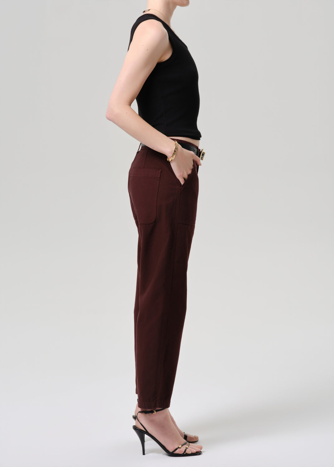 Person wearing a black sleeveless top and brown pants on a grey  background